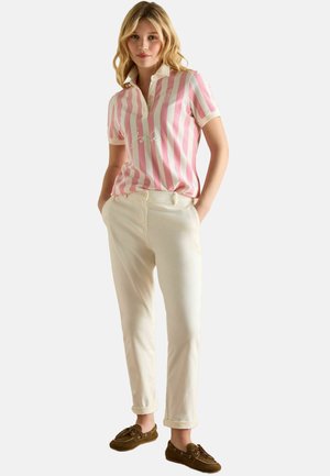 Hellrosa und weiße gestreifte Poloshirt mit Kragen und besticktem Detail, kombiniert mit cremefarbenen Hosen und braunen Schuhen.