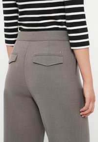 Szare dopasowane spodnie o gładkiej teksturze, z dwoma tylnymi kieszeniami i małym akcentem w postaci logo. Pas jest elegancki i strukturalny.