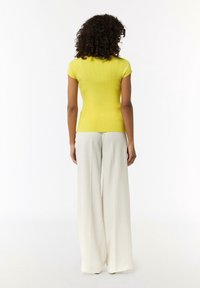 Gelbes, geripptes Kurzarmtop, kombiniert mit weißen, weiten Hosen, die ein figurbetontes Design und eine glatte Textur zeigen.