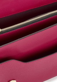 Magenta textured wallet with a smooth finish, featuring a gold-tone zipper and black trim. Interior has multiple compartments for organization.