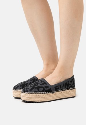 Černé espadrilky s tkanou juty, které mají texturovaný povrch a výrazné grafické černé písmo na svršku.