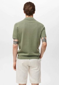 Camisa polo de punto acanalado en color verde oliva con mangas cortas, que presenta un diseño texturizado y una cintura ajustada; combinada con pantalones cortos color crema.