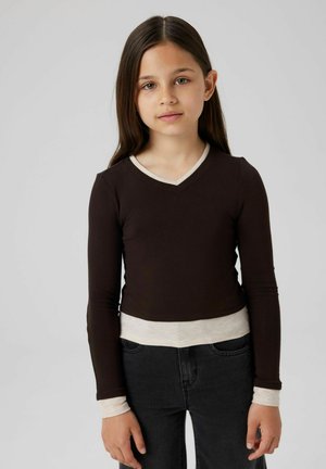 Camicia marrone a maniche lunghe con scollatura a V, con polsini e orlo color crema. Tessuto liscio, design aderente, abbinata a jeans scuri.