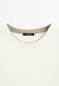 Witte T-shirt met een ronde halslijn. De kraag heeft een contrasterende beige rand. Label met het merk "Massimo Dutti" genaaid op de achterkant.