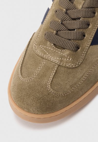 Oliiviroheline nahast sneaker pruunide paeltega, millel on kummist tald ja õmmeldud detailid, näidates minimalistlikku disaini.