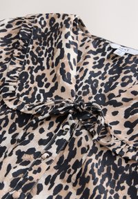 Blusa con stampa leopardata in tessuto setoso. Presenta un colletto arricciato, chiusura con laccio e bottoni neri sul davanti con schema di colori beige e nero.