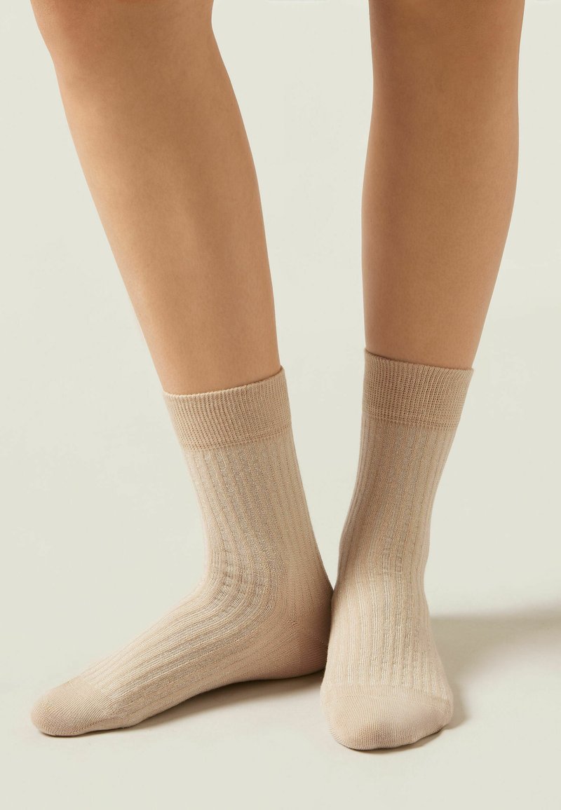 Beige gerippte Socken aus einem weichen, strukturierten Material. Mit einem dehnbaren Bündchen und einem glatten Strickkörper versehen, bieten sie einen bequemen Sitz.