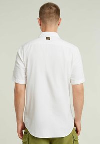 Camisa blanca de manga corta con un corte relajado, que presenta un dobladillo redondeado y una pequeña etiqueta de marca en la parte posterior del cuello. Tejido suave y ligero.
