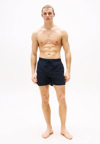 Μπλε βερμουδάκια κολύμβησης με ελαστική μέση και κορδόνι. Ελαφρύ ύφασμα, μήκος πάνω από το γόνατο, με μικρό λογότυπο στο κάτω μέρος.