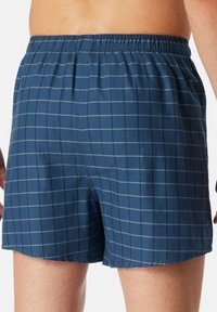 Boxer blu a quadretti con elastico in vita, presentano linee a griglia grigio chiaro e una morbida texture intrecciata. La vista posteriore mostra il termine dell'orlo.