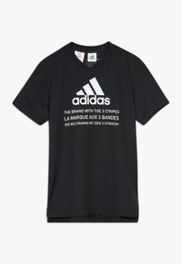 Svart bomull t-shirt med korta ärmar. Har vitt Adidas-logotyp och text på flera språk på framsidan. Slät textur.