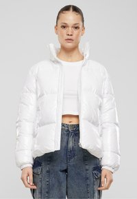 Hvit pufferjakke med blank finish, glidelås og høy krage. Kombinert med en kort hvit skjorte og vide denim-bukser.