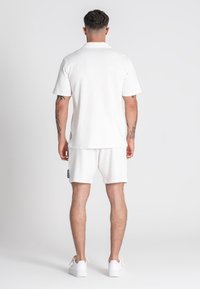 Polo de manga corta blanca y pantalones cortos a juego en tejido texturizado, con un corte relajado, y combinados con zapatillas blancas.