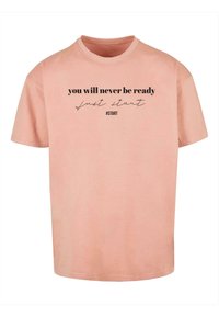 Lyserød bomulds T-shirt med korte ærmer og sort tekst: "du bliver aldrig klar, bare start #START" trykt foran.