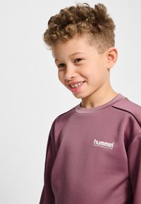 Lichtpaarse sweater gemaakt van gladde stof, met een ronde hals, lange mouwen en witte logotekst op de borst.