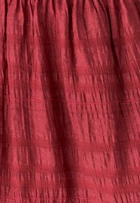 Rood gestructureerd stof met een gerimpeld ontwerp, voorzien van subtiele lijnen en plooien, wat een gelaagde uitstraling creëert. Ideaal voor kledingstukken of interieurdecoratie.