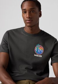 Dark gray cotton T-shirt with short sleeves, featuring a colorful circular graphic depicting mountains and the text "Levi's" in cream.