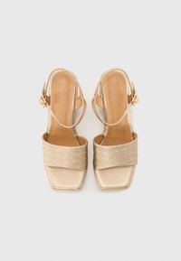 Sandales dorées à talon ouvert avec un bout carré texturé et une sangle supérieure à motif. Semelle lisse et sangle de cheville réglable pour un ajustement confortable.