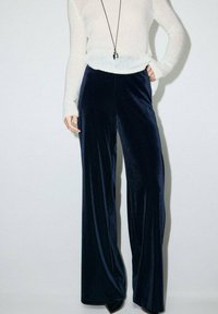 Pantaloni largi din catifea bleumarin cu o textură netedă, având un talie înaltă și o siluetă fluidă, asortați cu un pulover tricotat bej.
