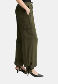 Pantalones de pierna ancha color verde oliva con cinturilla elástica, bolsillos laterales y lazos ajustables en los tobillos. Combinados con tacones negros de punta afilada.