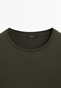 T-shirt vert olive foncé à col rond avec une étiquette visible au niveau du col indiquant « Massimo Dutti Made in China » sur un fond uni.