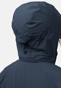 Veste imperméable bleu marine avec un col haut, une capuche réglable à cordon de serrage et un tissu lisse et texturé.