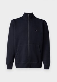 Sudadera con cremallera color navy, fabricada en una mezcla de algodón. Cuenta con un collar alto, bolsillos delanteros y un logo sutil en el pecho. Textura lisa, diseño casual.