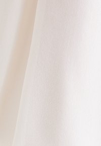 Gros plan d'un tissu lisse texturé de couleur blanc cassé avec des plis doux et une ombre subtile.