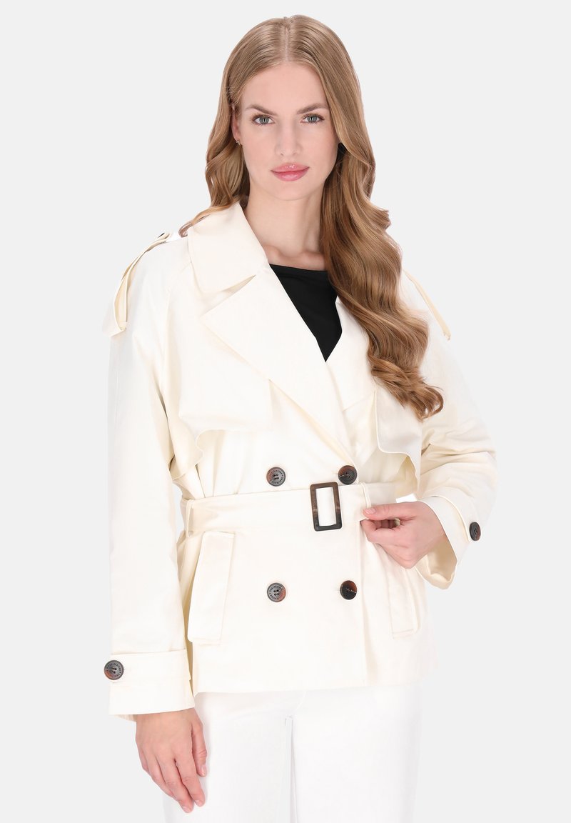 Krém színű ballonkabát dupla soros gombokkal, nagy gombokkal, övvel a deréknál és vállpántokkal. Simább, texturált anyag.