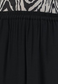 Jupe noire à taille élastique avec un haut imprimé zèbre noir et blanc visible au-dessus de la taille.