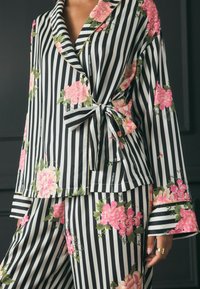 Pajama set s crno-bijelim prugama i cvjetnim ružičastim detaljima, s preklopnim dizajnom, vezanjem u struku i zvonastim rukavima. Mekana tkanina.