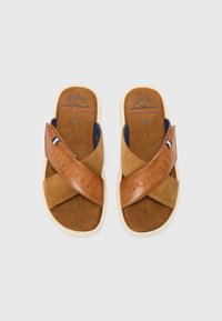 Sandales en cuir suédé et cuir marron avec des brides croisées, semelle beige, et logo "bugatti" embossé sur le cuir. Semelle intérieure texturée.