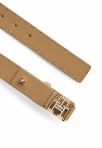 Cintura in pelle marrone chiaro con fibbia in metallo dorato che presenta un design geometrico del logo. Dettagli di cucitura lungo i bordi, texture liscia.