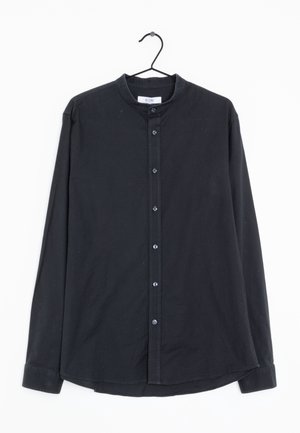 Sort langærmet skjorte med knapper og ståkrave, hængende på en sort bøjle mod en hvid baggrund.
