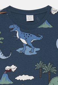 Blaues Baumwoll-T-Shirt mit einem grafischen Design, das einen blauen Dinosaurier, Berge, Bäume und Wolken in leuchtenden Farben zeigt. Runde Halslinie.