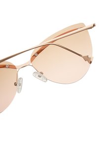 Růžové cat-eye sluneční brýle s tenkým kovovým rámem, průhlednými nosními podložkami a ostrým vrcholem v oblasti obočí. Hladký povrch.