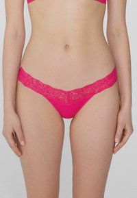 Rosa Spitzenstrings mit einem floralen Muster am Bund, glattem Stoff und minimalem Schnitt.