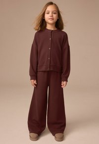 Bordowa prążkowana bluza dzianinowa z zaokrąglonym kołnierzem i zapięciem na guziki, zestawiona z szerokimi spodniami. Miękka tekstura i luźny krój.