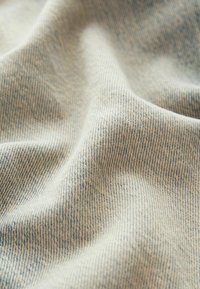 Tessuto di denim chiaro con una consistenza morbida, caratterizzato da un delicato motivo intrecciato blu e bianco. La superficie è leggermente stropicciata, mostrando profondità.