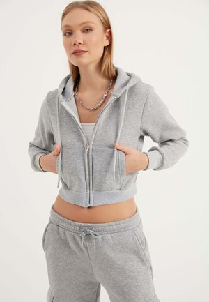 Grijze cropped hoodie met een rits aan de voorkant, trekkoorden en voorzakken. Zachte stof met een subtiele textuur. In combinatie met bijpassende joggingbroek.