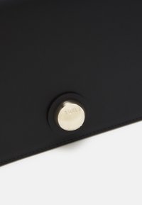 Czarna skórzana torba z okrągłym metalowym zapięciem z wygrawerowanym logo. Gładka faktura i starannie wykonane szwy tworzą minimalistyczny design.