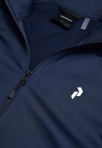 Giacca zip-up blu marina realizzata in tessuto liscio, con colletto alto, chiusura lampo visibile e logo bianco sul lato sinistro.