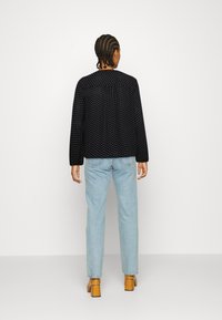 Casaco preto com bolinhas, de mangas longas e corte descontraído, combinado com jeans azul claro e sapatos de salto bloco bege.