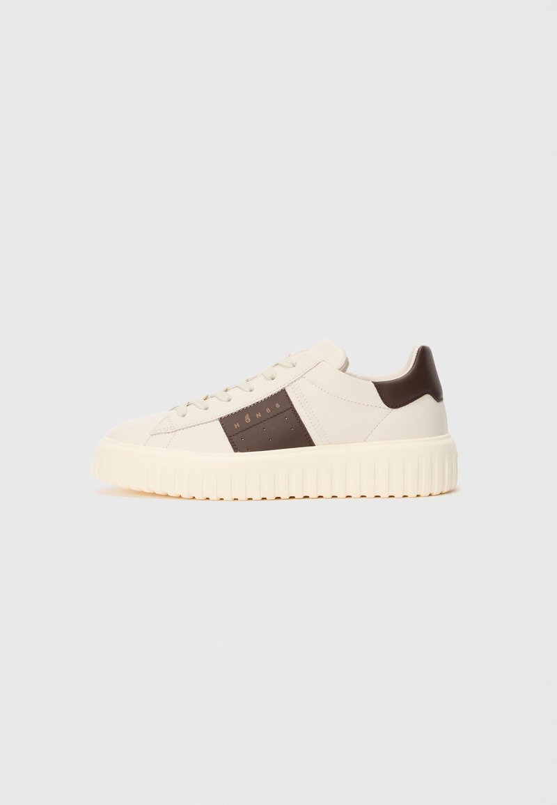 Sneaker bassa color crema con suola spessa e scanalata, tassello posteriore marrone e pannello laterale marrone con piccole perforazioni e testo "HØN86".