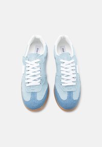 Ζευγάρι ανοιχτό μπλε τζιν αθλητικά παπούτσια με λευκά κορδόνια και σόλες από καουτσούκ καμήλας, εμφανιζόμενα από πάνω σε λευκό φόντο.