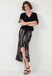 Blusa negra de lazo frontal combinada con una falda gris y negra con un dobladillo ondulado y rayas sutiles, complementada con sandalias negras de tiras.