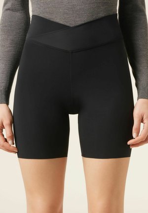 Schwarze Biker-Shorts mit hoher Taille und überkreuztem Bund, kombiniert mit einem figurbetonten grauen Langarmshirt, dargestellt von der Mitte des Oberschenkels bis zur Taille.