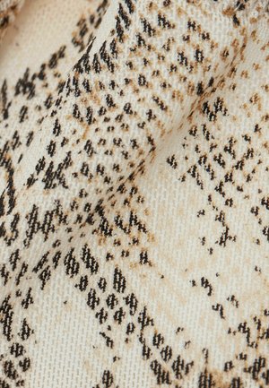 Snyggt ormskinnsmönstrat tyg med en texturerad beige bakgrund och svarta och bruna prickar som skapar ett mönster liknande reptilhud.