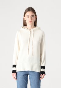 Krémová mikina s rebrovaným lemom a šnúrkami. Obsahuje čierno-biele prúžkované akcenty na rukávoch. Mäkký pletený materiál.