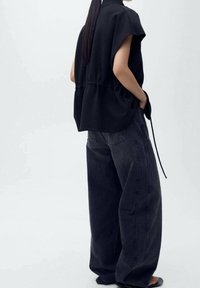 Haut noir à manches courtes avec taille cintrée, associé à un jean gris foncé à jambes larges et coupe ample. Tissu lisse avec une texture subtile.